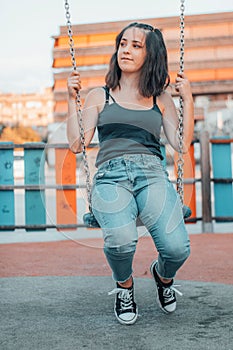 Vertical view of a beautiful young girl sitting on a swing while staring off into the distance