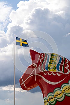 Vertical view of a colorful Swedish Dala horse and the Swedish flag under an expressive sky photo