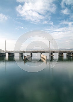 Vertical view of a concrete bridge over water with a train line and road running parallel and a boat and ship passageway below