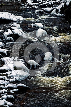 Vertical view of the foamy waves of a river flowing down the rocks in daylight in a forest