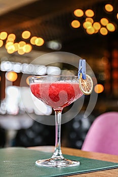 Vertical view of a glass of red alcohol cocktail with a dry tangerine dressing on the bar counter