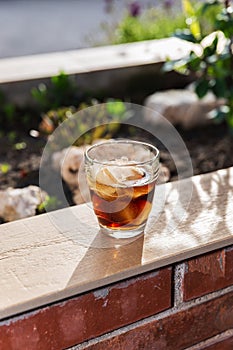 Vertical view of a glass of soft drink with ice on a wallflower outdoors, at sunset in summer. Copy Space. photo