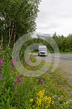 Vertical view of a gray camper van parked in the middle of nowhere in a gravel lot in the wilderness of northern Norway