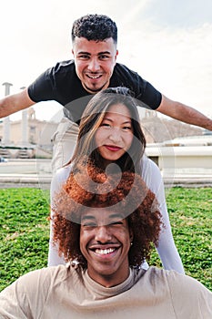 Vertical view of group of three multiracial young friends having fun and smiling looking at camera. Front view of happy