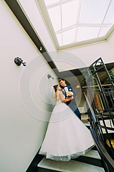 The vertical view of the happy newlyweds standing on the stairs.