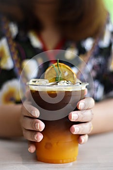 Vertical view, Iced coffee mixed with orange juice in a tall glass with a woman hand.