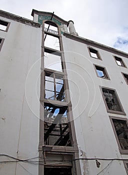 Vertical view of a large abandoned factory building with a tall chimney visible inside the ruins