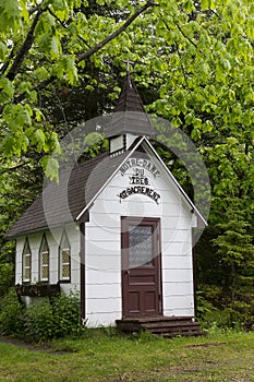 Vertical view of minuscule old brown and white wooden rural chapel nestled in tree