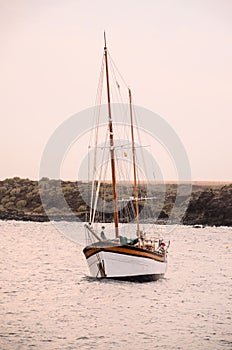 Vertical view of an old sailboat on the water before the cost under the pink sky