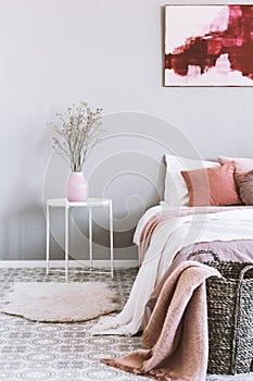 Vertical view of pink and grey bedroom interior with wicker basket and flowers in vase