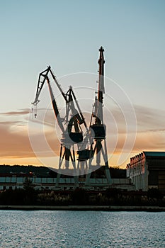 Vertical view of port shipyard cranes against sunset sky