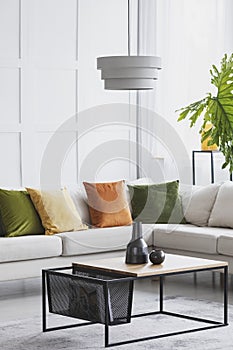 Vertical view of simple white chandelier hanging above modern wooden coffee table in living room with golden lime accents