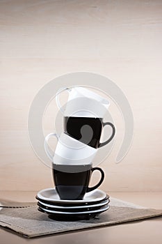 Vertical view of standing black and white cups on the stack of the plates on newspaper.