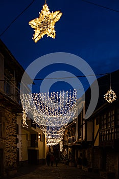 Vertical view of a street illuminated at Christmas with a star and lights, background with people walking between the stone houses