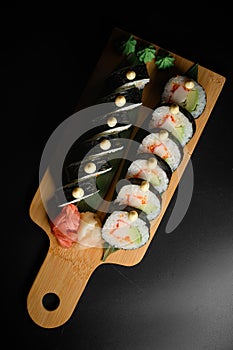 Vertical view of tasty sushi roll futomaki with avocado and crab meat on wooden serving board on black background.