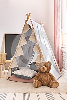 Vertical view of teddy bear next to tent with pillows in cute child`s playroom, real photo