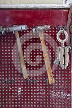 Vertical view of two old hammers with a brown wooden handle and a clamp hanging on the wall in a workshop for carpentry work on a