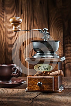 Vertical view vintage wooden coffee mill with little scoop and cup on wood background