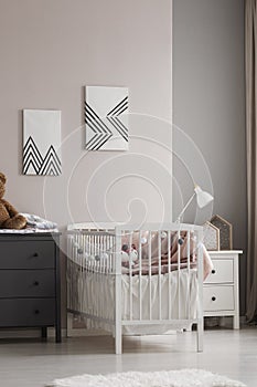 Vertical view of white crib with pastel pink bedding and cotton balls in grey and beige fashionable baby bedroom