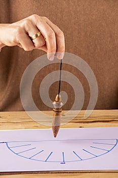 Vertical view of a woman`s hand holding a wooden pendulum over an energy curve,