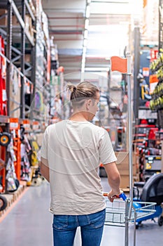 Vertical view of young man pushing a shopping cart in the corridor of an industrial hardware store