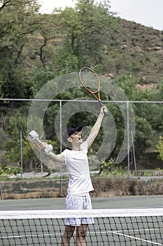 Vertical view of young tennis athlete enjoying his victory with happy and excited face expresion. Holding a cup