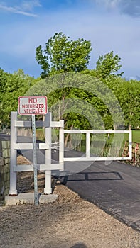 Vertical White gate and sign post on a narrow road with grassy field and trees background