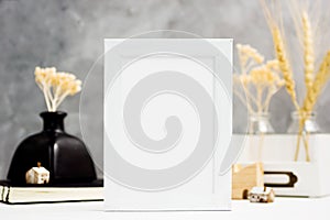 Vertical white Photo frame mock up with dry plants in vase, notebook and wooden houses on shelf. Scandinavian style