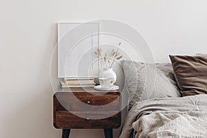 Vertical white picture frame mockup on old books. Elegant bedroom view. Brown, grey linen and velvet pillows, blanket