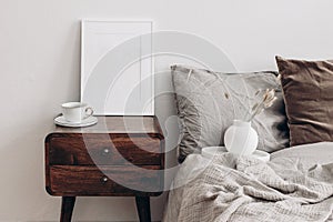 Vertical white picture frame mockup. Retro wooden bedside table. Modern white ceramic vase with dry Lagurus ovatus grass