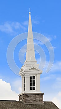 Vertical White steeple on top of the pitched roof of a church with brick exterior wall