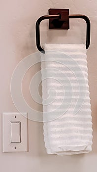 Vertical White towel hanging on square towel holder beside electrical rocker light switch