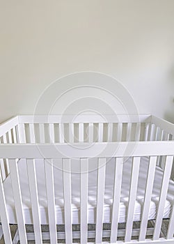 Vertical White wooden crib with white mattress in a white carpeted room