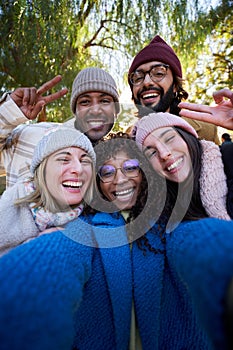 Vertical. Winter time smiling selfie of a happy group of multicultural friends looking at the camera