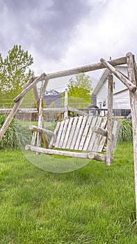 Vertical Wooden bench swing at the lush grassy yard of a home with white picket fence