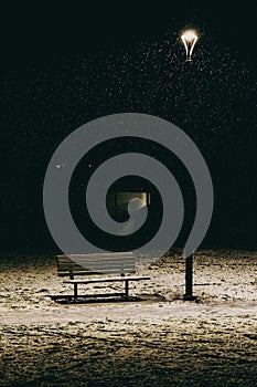 Vertical of a wooden bench under a streetlamp at night in snow