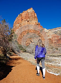 VERTICAL: Young woman treks along a dirt trail under the sandstone mountain