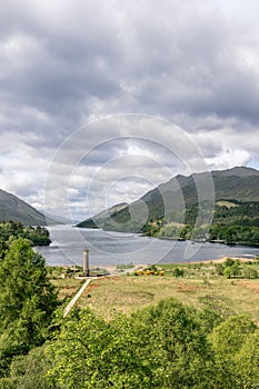 Vertically framed Glenfinnan Monument rises by Loch Shiel, guiding eyes to distant Highlands under a wide sky