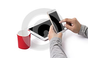 Vertically held white phone in man`s hands. A red cup and an Ipad on the white table