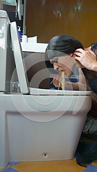 vertically. a man disguised as a woman eating noodles from the toilet