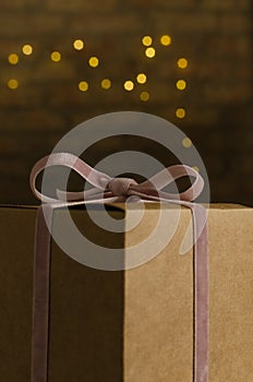 Verticl image.Craft paper box and pink ribbon, bow against christmas lights bokeh on the brick wall