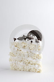 Verticl image.Piece of biscuit cake with glaze, chocolate cookie crumbs and whole round sandwich cookie