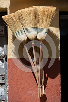 Verticl shot of a set of brooms hanging on the wall under the sunlight