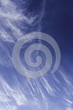 Verticle white cirrus clouds moving to cover blue sky photo