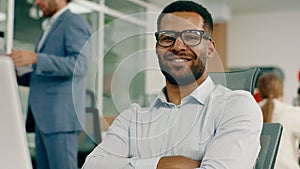 A very alluring manager is sitting at his desk in the big office wearing black glasses as he does his work on the laptop