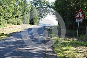 very bad road with crumbling edge and warning sign for bad road