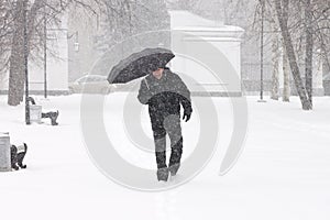 Very bad weather in a city in winter: terrible heavy snowfall and blizzard. Male pedestrian hiding from the snow under umbrella