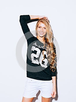 Very beautiful girl with long blond hair posing on a white background. She raised her hand above her head and smiling. Sweatshirt