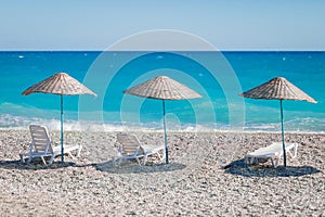 Very beautiful view of the beach with pebbles and the blue ocean or the azure sea with white sun loungers and wicker umbrellas.