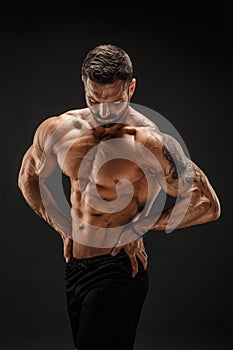 Bodybuilder posing. Fitness muscled man on dark background.